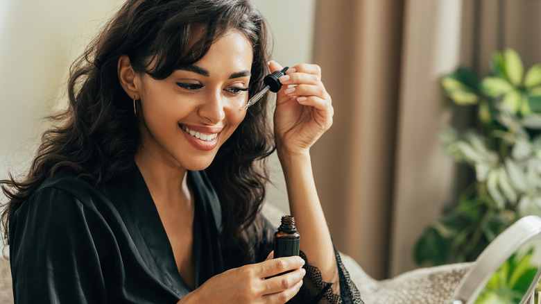 Young smiling woman sitting on a couch applying hyaluronic acid on a face